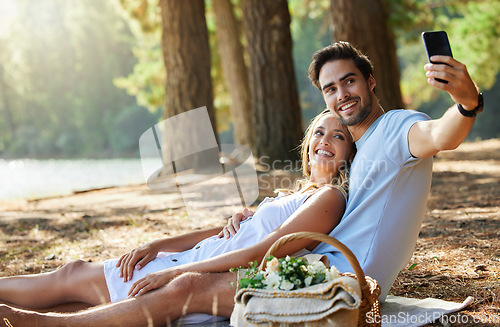 Image of Couple, relax and smile for picnic selfie in the forest on holiday break or romantic summer vacation together. Happy man and woman relaxing or smiling on mat for photo, memory or date in nature