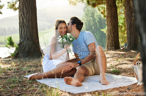 Image of Couple kiss, love and flowers on picnic, summer with freedom and adventure, affection in relationship and care outdoor. Happy people together in nature, commitment and trust with romance in forest