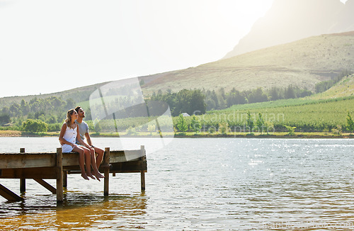 Image of Couple in nature, relax by lake and summer, travel and adventure, love and care outdoor. People in relationship, trust and bond on vacation, man and woman together sitting on jetty, freedom and view