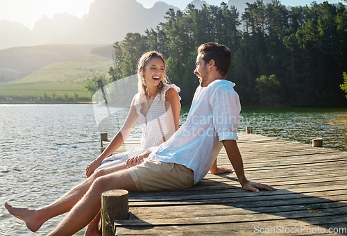 Image of Love, laugh and pier with couple at lake for bonding, romance and affectionate date. Nature, travel and holiday with man and woman sitting on boardwalk in countryside for happy, summer and vacation