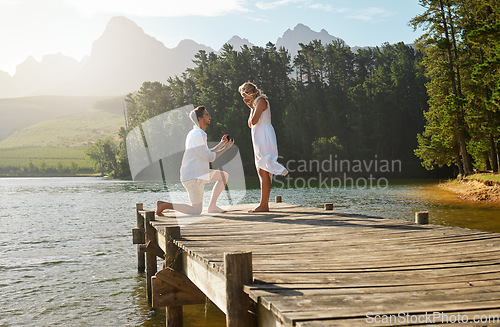 Image of Man, woman and engagement proposal by lake on vacation with surprise, wow or happiness in sunshine. Couple, marriage offer and ring in nature for romance, love and happy on holiday in summer by water