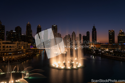 Image of Dubai singing fountains at night lake view between skyscrapers. City skyline in dusk modern architecture in UAE capital downtown.