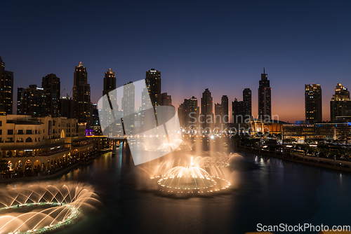 Image of Dubai singing fountains at night lake view between skyscrapers. City skyline in dusk modern architecture in UAE capital downtown.