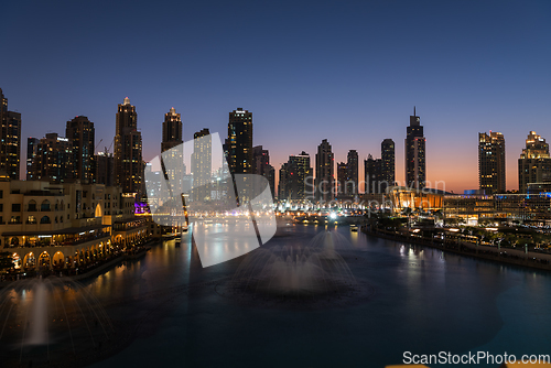 Image of Dubai singing fountains at night lake view between skyscrapers. City skyline in dusk modern architecture in UAE capital downtown.