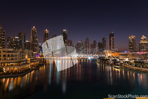 Image of Dubai singing fountains at night lake view between skyscrapers. City skyline in dusk modern architecture in UAE capital downtown.