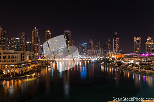 Image of Dubai singing fountains at night lake view between skyscrapers. City skyline in dusk modern architecture in UAE capital downtown.