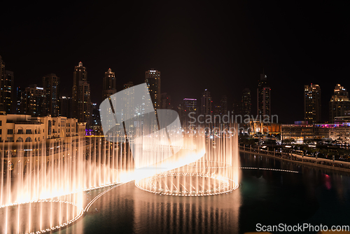 Image of Dubai singing fountains at night lake view between skyscrapers. City skyline in dusk modern architecture in UAE capital downtown.