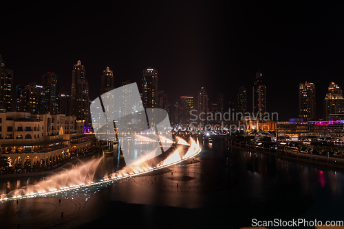 Image of Dubai singing fountains at night lake view between skyscrapers. City skyline in dusk modern architecture in UAE capital downtown.