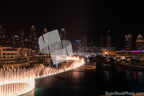 Image of Dubai singing fountains at night lake view between skyscrapers. City skyline in dusk modern architecture in UAE capital downtown.