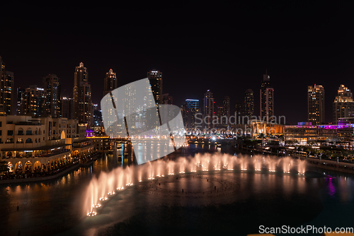 Image of Dubai singing fountains at night lake view between skyscrapers. City skyline in dusk modern architecture in UAE capital downtown.