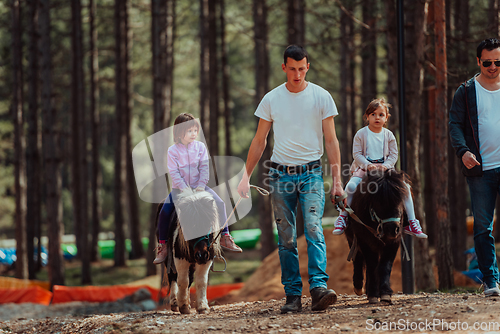 Image of Two little girls having fun in the park while riding small horses