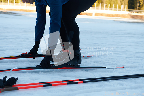 Image of Handsome male athlete with cross country skis preparing equipment for training in a snowy forest. Checking smartwatch. Healthy winter lifestyle.