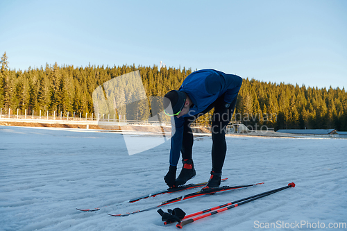 Image of Handsome male athlete with cross country skis preparing equipment for training in a snowy forest. Checking smartwatch. Healthy winter lifestyle.