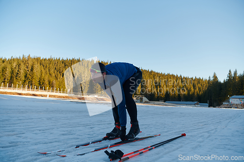 Image of Handsome male athlete with cross country skis preparing equipment for training in a snowy forest. Checking smartwatch. Healthy winter lifestyle.