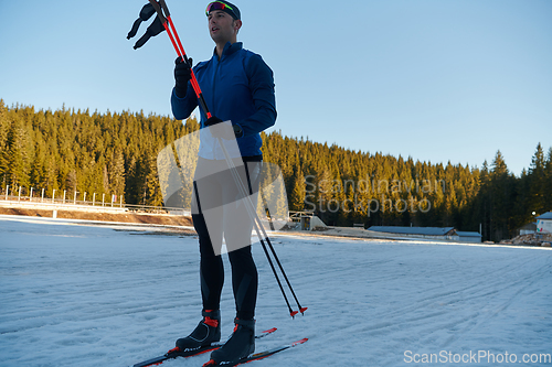 Image of Handsome male athlete with cross country skis preparing equipment for training in a snowy forest. Checking smartwatch. Healthy winter lifestyle.