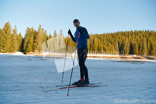 Image of Handsome male athlete with cross country skis preparing equipment for training in a snowy forest. Checking smartwatch. Healthy winter lifestyle.