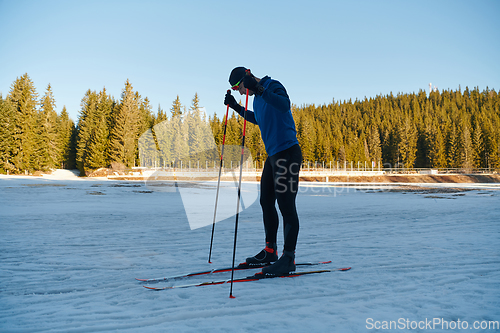 Image of Handsome male athlete with cross country skis preparing equipment for training in a snowy forest. Checking smartwatch. Healthy winter lifestyle.