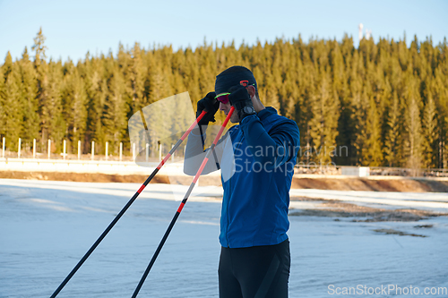 Image of Handsome male athlete with cross country skis preparing equipment for training in a snowy forest. Checking smartwatch. Healthy winter lifestyle.