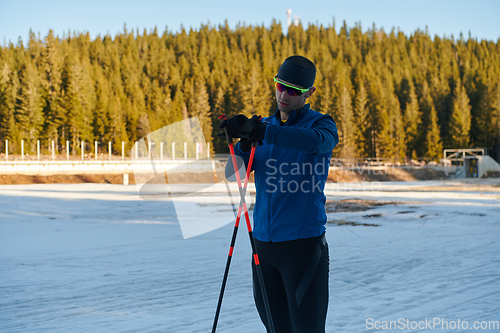 Image of Handsome male athlete with cross country skis, taking fresh breath and having break after hard workout training in a snowy forest. Checking smartwatch. Healthy winter lifestyle