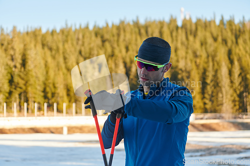 Image of Handsome male athlete with cross country skis, taking fresh breath and having break after hard workout training in a snowy forest. Checking smartwatch. Healthy winter lifestyle