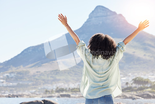 Image of Woman at beach, arms in air and freedom, back view with mountains and travel, praise and sunshine. Female person outdoor, carefree and adventure, mindfulness and peace with worship in nature