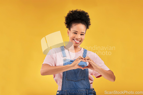 Image of Hands, black woman and sign for a heart, love and portrait of care or support on yellow background in studio. Happy, face and girl with hand gesture for loving, kindness or emoji for caring mindset