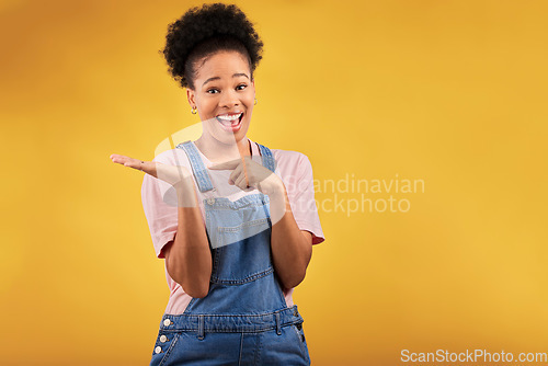 Image of Portrait, space and a black woman pointing to her palm for the promotion of a product on a yellow background in studio. Smile, advertising or marketing with a happy young female brand ambassador