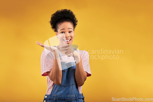 Image of Portrait, marketing and a black woman pointing to her palm for the promotion of a product on a yellow background in studio. Smile, advertising or space with a happy young female brand ambassador