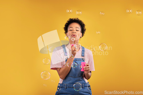 Image of Woman, blowing bubbles and fun in studio while playful for birthday, happiness or party celebration. Black female model person with liquid soap, natural beauty and fashion on a yellow background