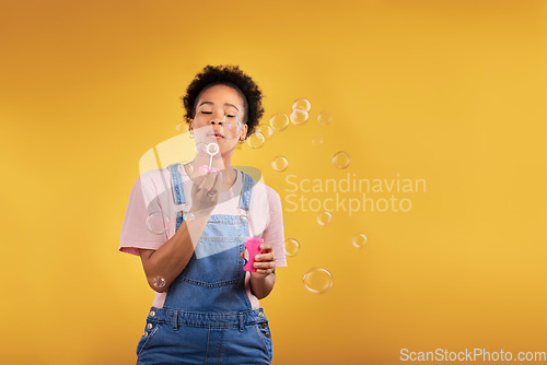 Image of Blowing bubbles, woman and fun in studio while playful for birthday or party celebration. Black female model person with liquid soap, natural beauty and fashion on a yellow background with space