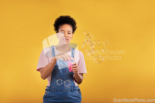 Image of Woman, blowing bubbles and fun portrait in studio while playful for birthday, space or party celebration. Black female model person with liquid soap, natural beauty and fashion on a yellow background