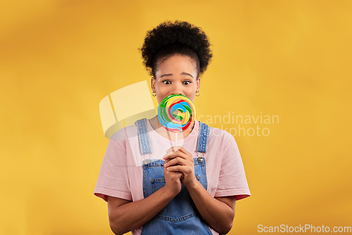 Image of Portrait, black woman with candy or lollipop in studio on yellow background and eating sweets, dessert or food with sugar. Gen z, face of girl and hungry for delicious treats, snack or product