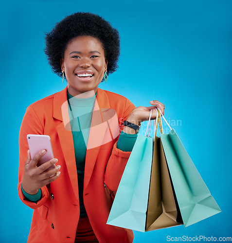 Image of Shopping bag, phone and happy woman for e commerce sale, discount or social media on blue background. Portrait, mobile blog and fashion of african person, customer or online user with gift in studio