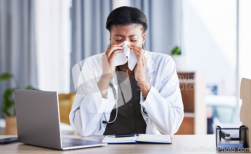 Image of Sick, doctor and a black woman blowing nose in an office as a healthcare employee at a desk. Table, hospital and an African nurse or medical worker sneezing into a tissue with a virus or flu