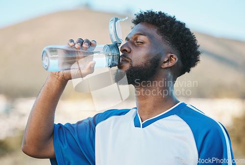 Image of Black man, fitness or soccer player drinking water in training, exercise or workout in football field. Thirsty, sports or tired athlete on resting break with a healthy beverage for energy to relax