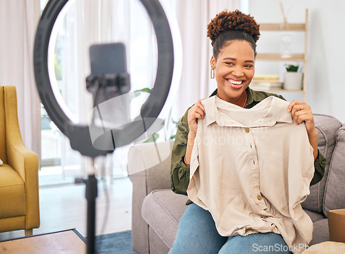 Image of Fashion, live streaming and a black woman influencer unboxing a clothes outfit in her home. Social media, brand deal and a happy female content creator recording a broadcast for subscription service