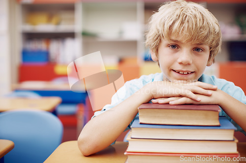 Image of So much to learn. A happy young boy sitting at his desk and leaning his chin on a stack of books.