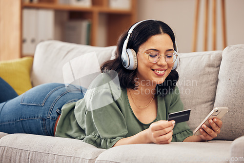 Image of Woman, credit card and phone on sofa, home and headphones with smile, online shopping or payment on web. Girl, smartphone and fintech app for cybersecurity, discount and deal with e commerce store