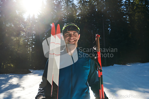 Image of Portrait handsome male athlete with cross country skis in hands and goggles, training in snowy forest. Healthy winter lifestyle concept.