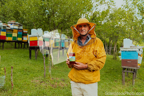 Image of The beekeeper holding a jar of honey in his hand while standing in a meadow surrounded by a box and a honey farm