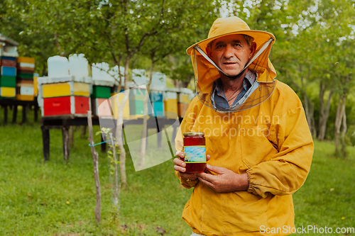 Image of The beekeeper holding a jar of honey in his hand while standing in a meadow surrounded by a box and a honey farm