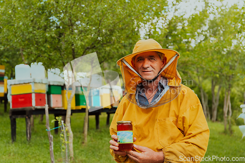 Image of The beekeeper holding a jar of honey in his hand while standing in a meadow surrounded by a box and a honey farm