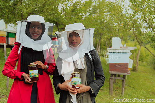 Image of Portrait of an Arab investors holding a jar of honey in their hands while standing in front of a large honey farm. The concept of investing in small businesses