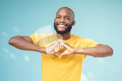 Image of Hand, heart and portrait of man in studio for love, happy and smile against a blue background space. Emoji, hands and face of male model relax with finger, frame and loving message, gesture and sign