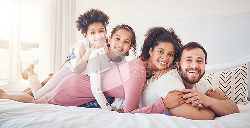 Image of Interracial, happy family and portrait on a bed, bond and having fun on the weekend in their home together. Relax, love and face of playful children with parents in a bedroom, smile and playing games