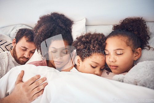 Image of Family, sleeping and together in bed at home for security, bonding and comfort. Healthy, mixed race and a man, woman and children nap, dream and rest or relax in a bedroom with love, care and peace