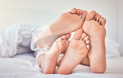 Image of Feet, love and a couple in bed to relax in the morning while bonding in their home for trust or support. Bedroom, sleeping or dreaming with a man and woman resting closeup under a blanket in a house