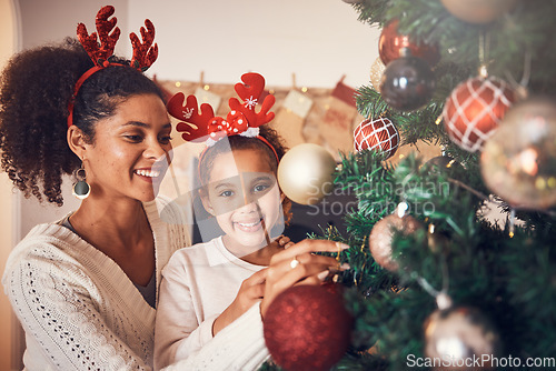 Image of Christmas, portrait and mother with girl decorating tree, bonding and happy together. Xmas, smile and face of kid with African mom with ornament for family party, celebration or holiday event in home