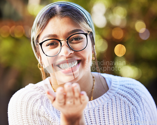 Image of Portrait, smile and blowing a kiss with a woman on a nature green background for love or romance. Face, glasses and flirt with a happy young female person standing in a garden on valentines day