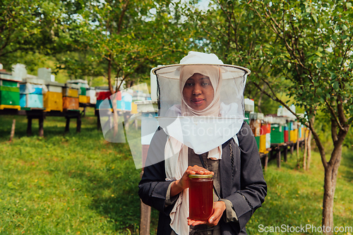 Image of Portrait of a Muslim African American woman in the beekeeping department of a honey farm holding a jar of honey in her hand